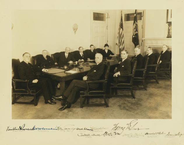 President Franklin Roosevelt seated with his ten cabinet members. From left to right: Franklin Delano Roosevelt, William Hartman Woodin, Homer Stille Cummings, Claud Augustus Swanson, Henry Agard Wallace, Frances Perkins, Daniel Calhoun Roper, Harold Leclair Ickes, James Aloysuis Farley, George Henry Dern, and Cordell Hull. All are turned in their seats to face the camera.