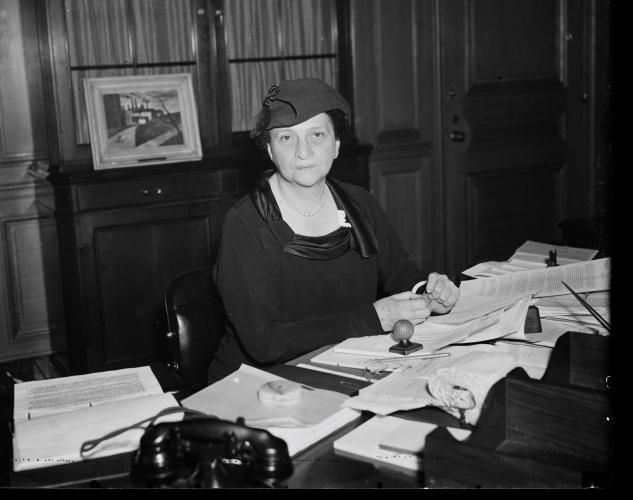 Black and white photo of Francis Perkins seated at a desk with papers scattered in front of her.